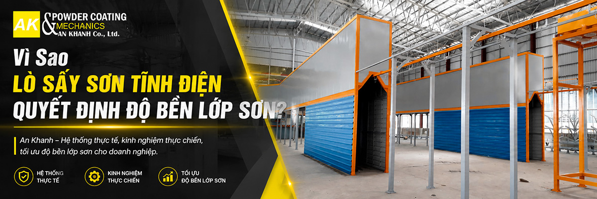 Lò sấy sơn tĩnh điện kiểu đường hầm vách panel xanh khung cam đặt trong nhà xưởng, cửa lò mở ở hai đầu cho băng tải treo đi xuyên qua