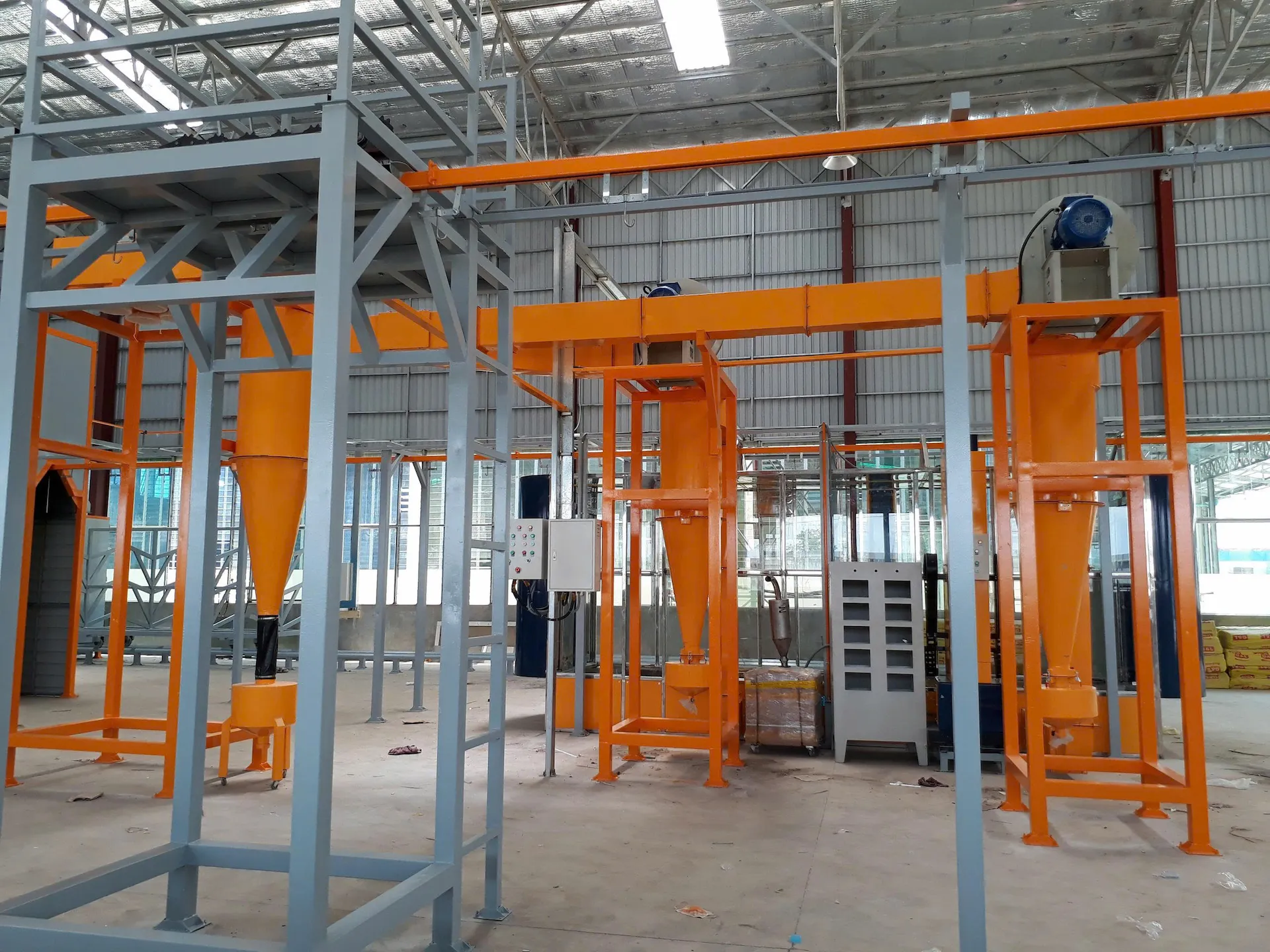 Ba cụm cyclone thu hồi bột màu cam đặt trên khung thép cao, mô tơ và quạt hút gắn trên đỉnh, ống dẫn nối về buồng phun phía sau và tủ điều khiển súng ở giữa